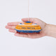 Craftspring’s Staten Island Ferry ornament held in front of a hand to show its size—handmade from sustainable wool with intricate embroidered details and beaded waves, featuring the iconic orange ferry, ethically crafted by artisans using sustainable wool.