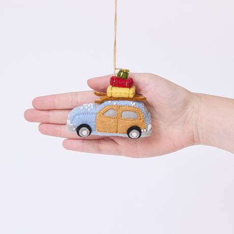 Craftspring’s Station Wagon with Luggage Ornament displayed in front of a hand to show its size — felt blue station wagon carrying suitcases, skis, and presents, with beaded snow details, a charming heirloom-quality piece for Christmas gifting — ethically crafted by artisans using sustainable wool.