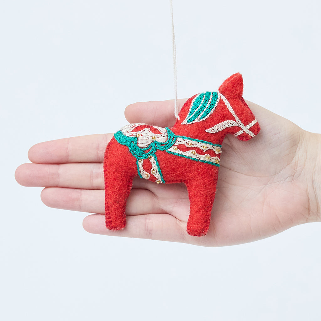 Craftspring’s Swedish Dala Horse Ornament displayed in front of a hand to show its size—handmade felt with detailed embroidery and beading, heirloom-quality Christmas ornament, perfect for holiday gifting, ethically handcrafted by artisans using sustainable wool.