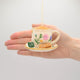 Hand-felted ornament of a floral teacup with a matching saucer, featuring embroidered golden rims, a tiny felt tea bag, and two sugar biscuits on the side. Crafted from merino-blend wool with fine needlework, the ornament includes a hanging string and measures approximately 1.5 inches high and 3.25 inches wide. A charming tribute to afternoon tea and cozy traditions