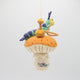 Hand-felted wool ornament of the Caterpillar from Alice in Wonderland, perched on a red-and-white mushroom with a hookah beside him. Features detailed embroidery and the phrase 'Who are you?' stitched at the base. Made from natural merino-blend wool, this whimsical ornament includes a hanging string and measures approximately 5.5 inches tall.