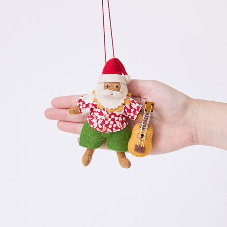 Craftspring’s Tropical Santa Ornament displayed in front of a hand to show its size — handmade from sustainable wool with embroidered details of Santa in an Aloha shirt holding a ukulele, ethically crafted by artisans.
