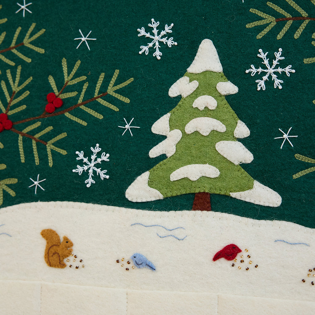 Craftspring’s Woodland Advent Calendar — handmade felt calendar with appliqué, embroidered, and beaded details of a snowy woodland scene featuring a snowy tree, birds, a squirrel, evergreen branches with red berries, and snowflakes — heirloom-quality Christmas decor, ethically crafted by artisans using sustainable wool.
