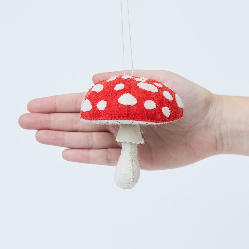Craftspring’s Woodland Amanita Mushroom Ornament displayed in front of a hand to show its size—handmade felt with applique and embroidered details, heirloom-quality Christmas ornament, perfect for holiday gifting, ethically handcrafted by artisans using sustainable wool.
