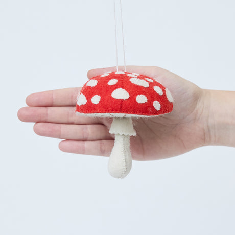 Craftspring’s Woodland Amanita Mushroom Ornament displayed in front of a hand to show its size—handmade felt with applique and embroidered details, heirloom-quality Christmas ornament, perfect for holiday gifting, ethically handcrafted by artisans using sustainable wool.