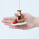 Craftspring’s Fox on Stump Ornament displayed in front of a hand to show its size—handmade felt fox on a stump with green present and red cardinal, heirloom-quality Christmas ornament, perfect for holiday gifting, ethically crafted by artisans using sustainable wool.
