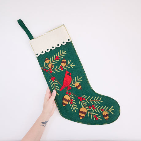 Craftspring’s Woodland Stocking ornament held in hand to show its size—handmade from sustainable wool with intricate applique and embroidered details, including a cardinal sitting on a pine branch, ethically crafted by artisans using sustainable wool.