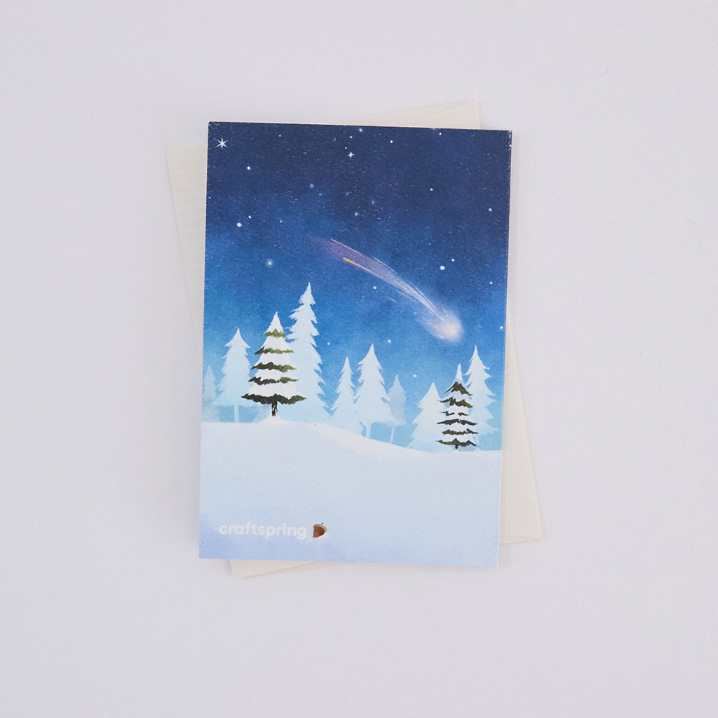 Back of Craftspring’s Woodland Tree Greeting Card, showing a snowy forest with a shooting star illustration, ethically printed in the USA on natural textured paper, perfect for sharing holiday cheer and gifting.