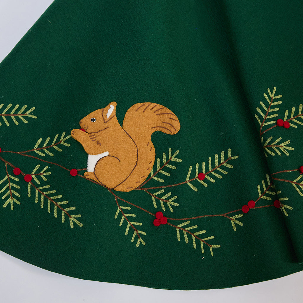 Close-up of Craftspring’s Woodland Tree Skirt showing an embroidered and appliqué squirrel nestled among pine branches and berries — festive holiday detail, handmade by artisans using sustainable wool.