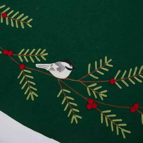 Close-up of Craftspring’s Woodland Tree Skirt showing embroidered and appliqué chickadees nestled in evergreens with red berries — heirloom-quality Christmas detail, handmade by artisans using sustainable wool.