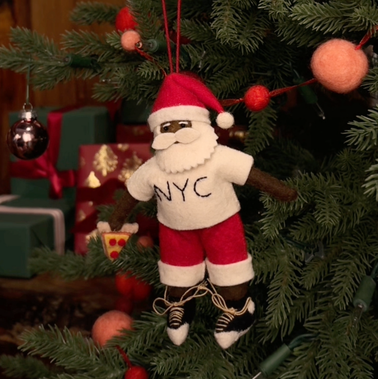 Celebrate Christmas in the Big Apple with our handmade NYC Santa Ornament, featuring a deep brown Santa dressed like a true New Yorker in an NYC tee and sneakers, with a classic slice of New York pizza in hand.