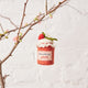 Hand-felted wool ornament of a strawberry jam jar, topped with a white gingham-style lid and a blooming felt strawberry. Features a stitched label and vibrant red detailing, evoking homemade summer preserves. Measures 3.25 inches tall and includes a hanging string — a charming gift for gardeners, bakers, or lovers of nostalgic, handmade summer treasures.