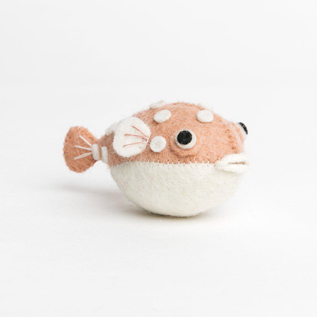 A handmade felt pufferfish ornament with a baby pink upper body and white spots and fins and a white belly.