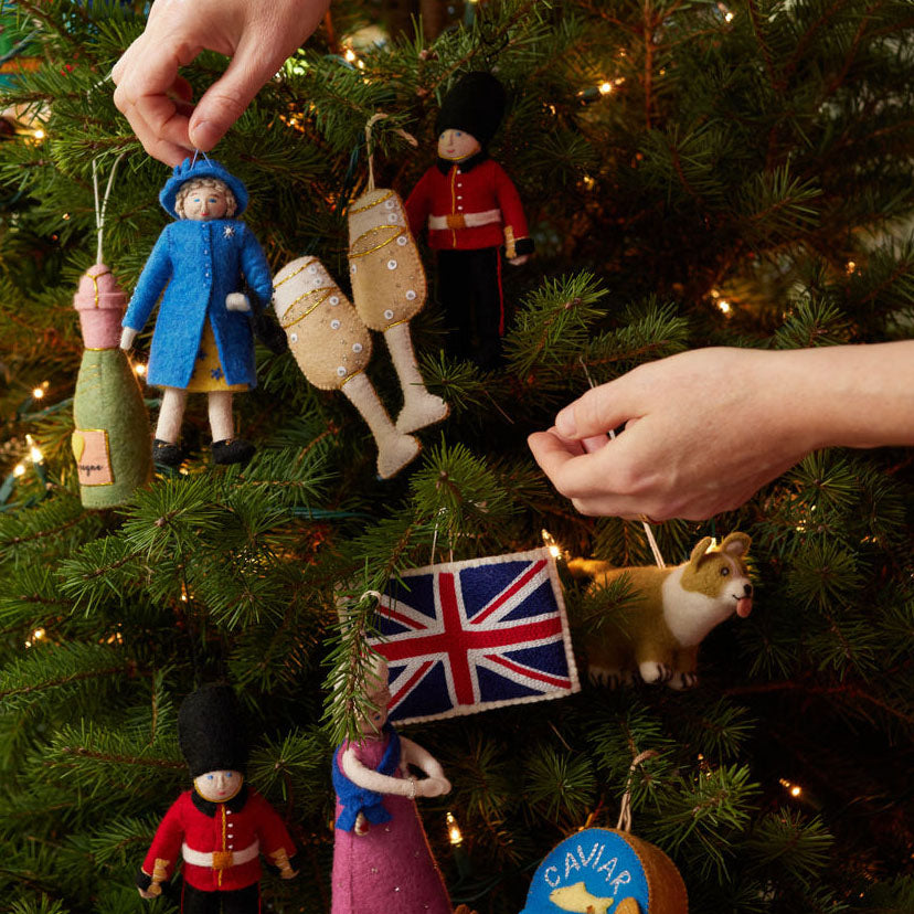 Queen Elizabeth II felt ornament wearing royal blue coat and hat, with black handbag and detailed embroidery. Handmade wool Christmas ornament honoring British royalty. Fair trade and ready to hang.  On a christmas tree.