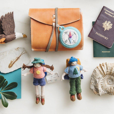 A handmade felt hiker ornament with light skin wearing brown hiking boots green cargo pants a blue shirt and cap with a brown backpack complete with bed roll.