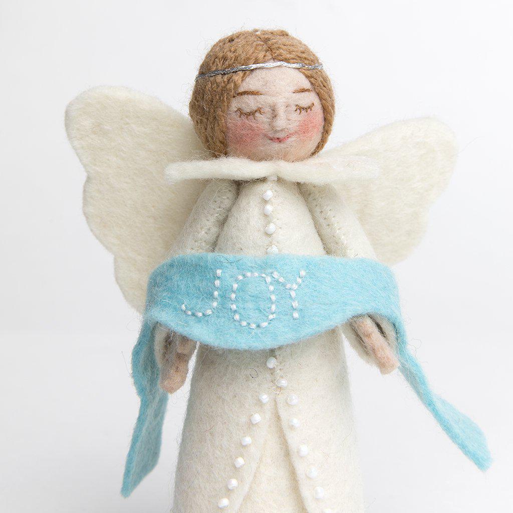 A craftspring handmade felt angel ornament wearing white robes and holding a blue banner with the word joy embroidered across it