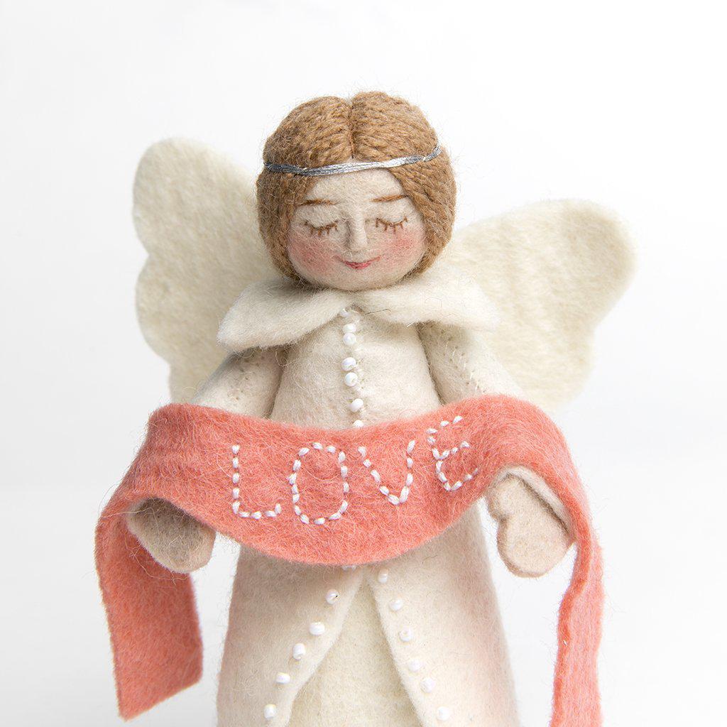 A craftspring handmade felt angel ornament wearing white robes and holding a pink banner with the word love embroidered across it