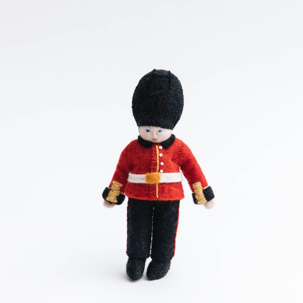 Queen’s Guard felt ornament wearing red coat and black bearskin hat, inspired by Buckingham Palace guards. Handmade wool Christmas ornament celebrating British tradition. Fair trade and ready to hang.