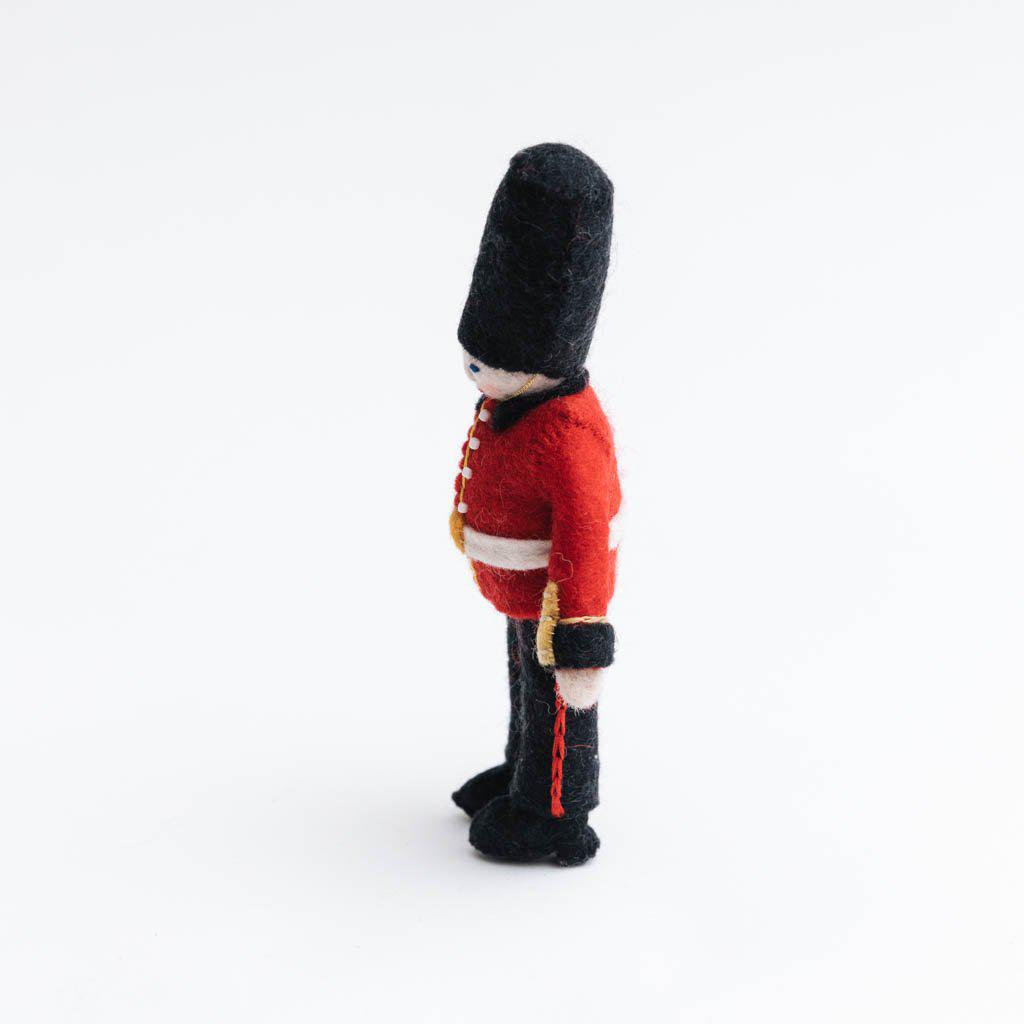Queen’s Guard felt ornament wearing red coat and black bearskin hat, inspired by Buckingham Palace guards. Handmade wool Christmas ornament celebrating British tradition. Fair trade and ready to hang. side view