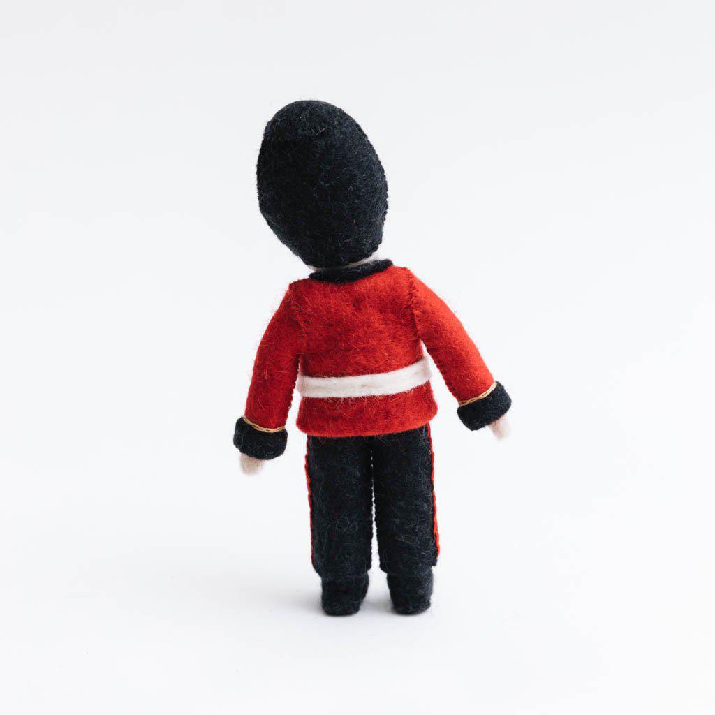 Queen’s Guard felt ornament wearing red coat and black bearskin hat, inspired by Buckingham Palace guards. Handmade wool Christmas ornament celebrating British tradition. Fair trade and ready to hang. back view